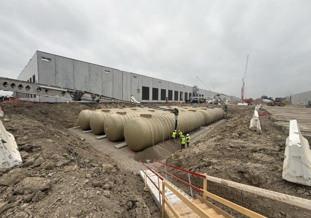 Crew setting fiberglass fuel storage tanks in an excavation beside a data center