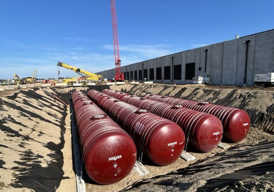 Row of red steel generator fuel tanks in an excavation beside a data center