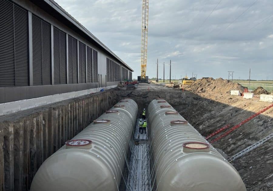 Two fiberglass fuel tanks set in a shored trench alongside a data center building